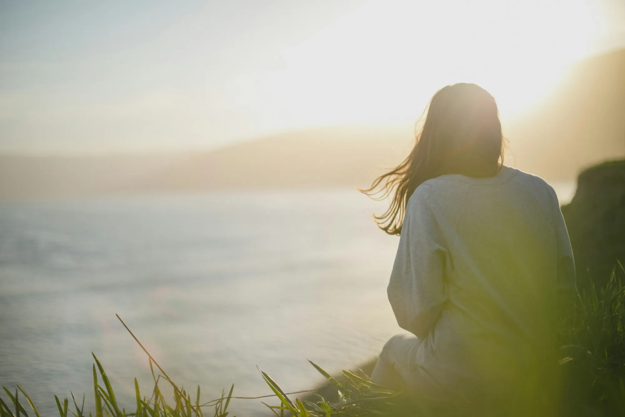 A woman sitting alone by the water, looking out at the horizon