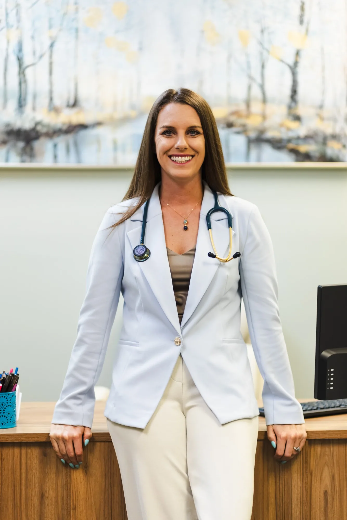 Sara McCalley, FNP-C, smiling in a light blue blazer with a stethoscope in her office